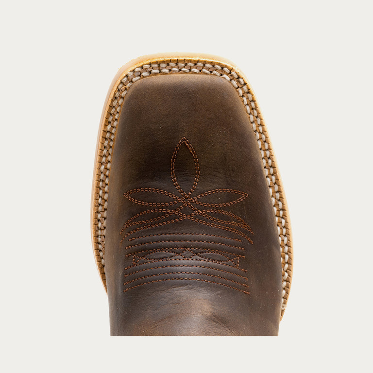 Close-up of a brown leather boot with intricate stitching on a light gray background