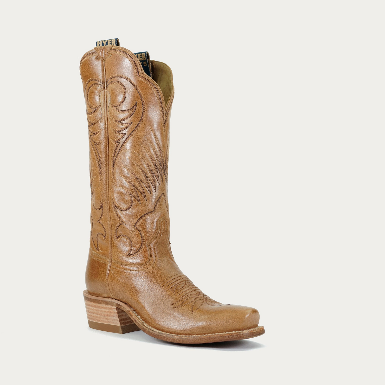 A brown, smooth leather cowboy boot with intricate embossing and a low heel.