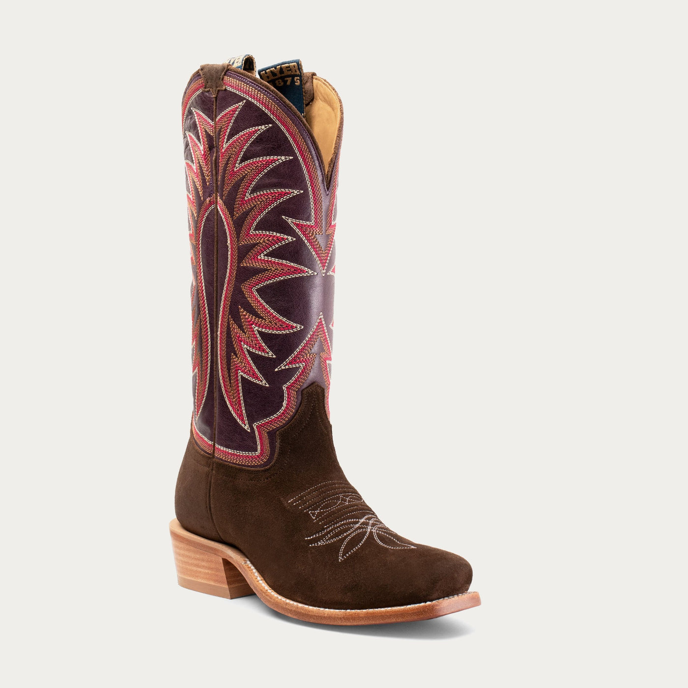 A brown cowgirl boot with red and black stitching pattern on the top section and a low heel.