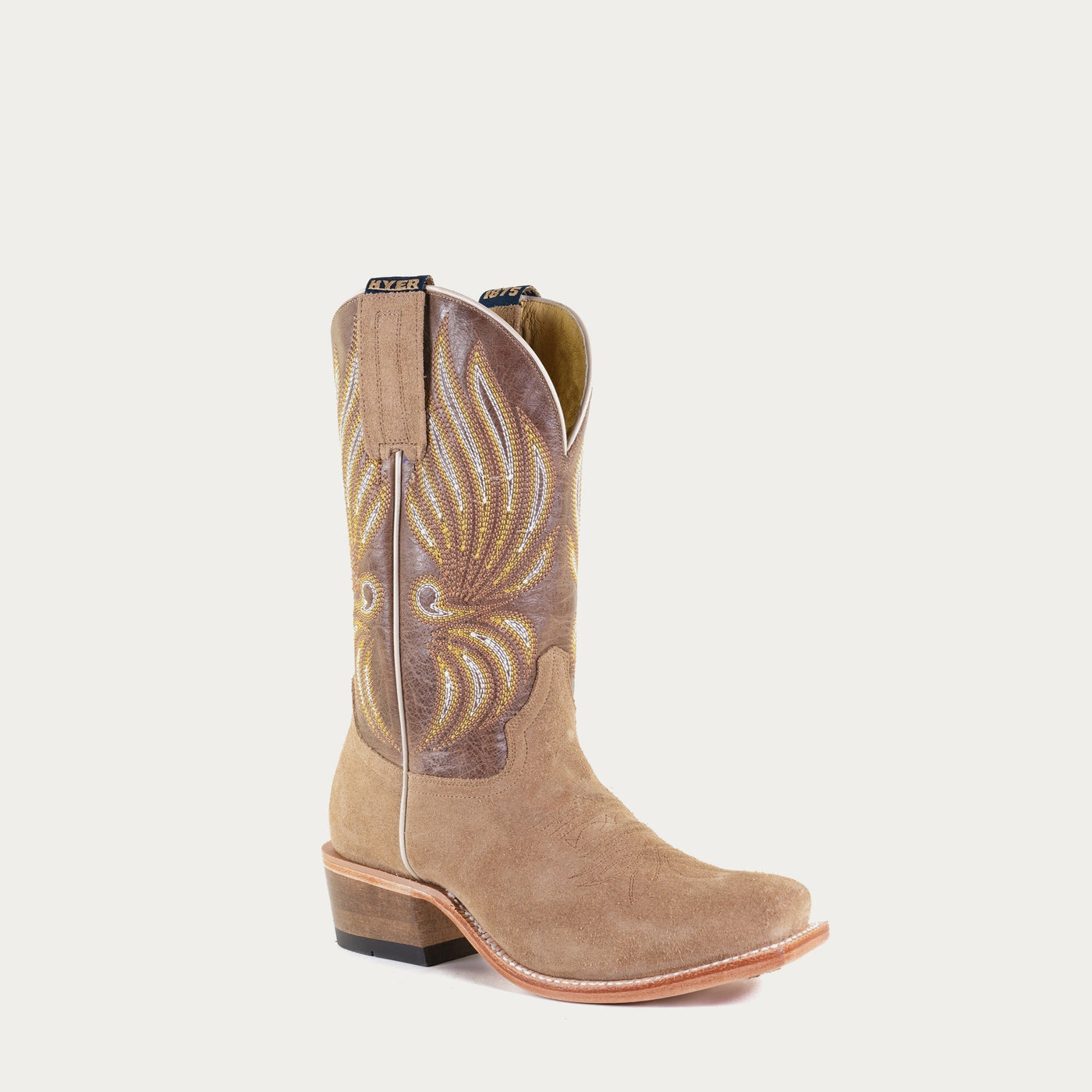 A brown leather cowgirl boot with a decorative design on the upper and tan suede on the vamp