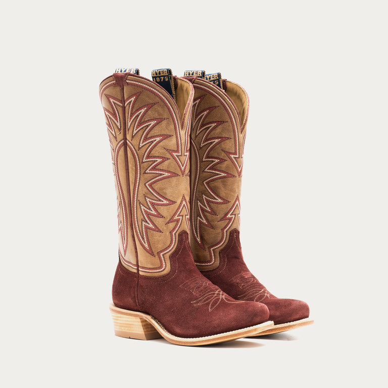 Pair of burgundy and tan cowboy boots with intricate designs on a gray background