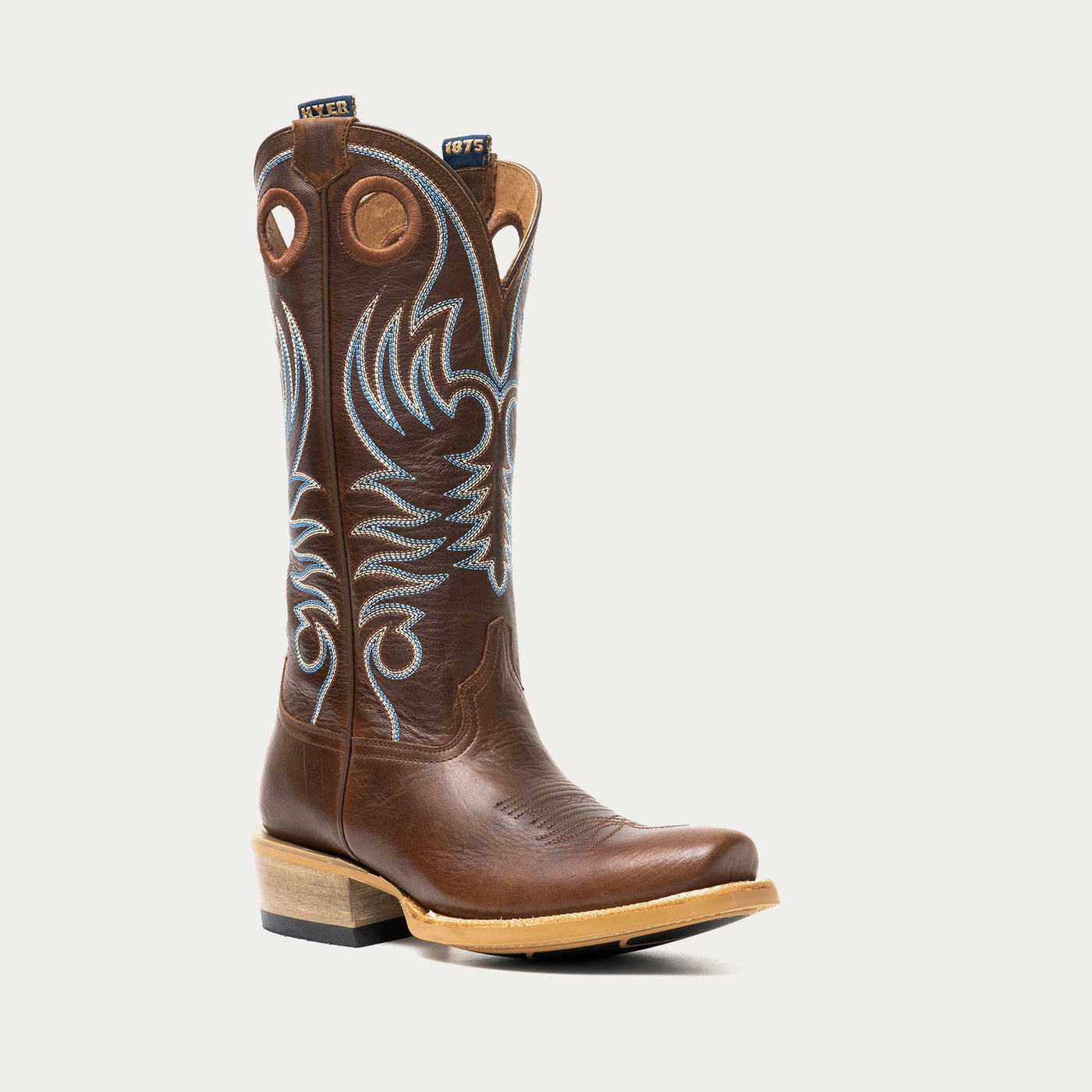 Brown cowboy boot with intricate white and blue embroidery on a light gray background