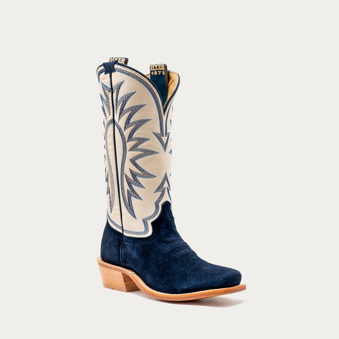 A single western cowboy boot in navy blue suede with a cream shaft featuring blue embroidered stitching, set against a light gray background.