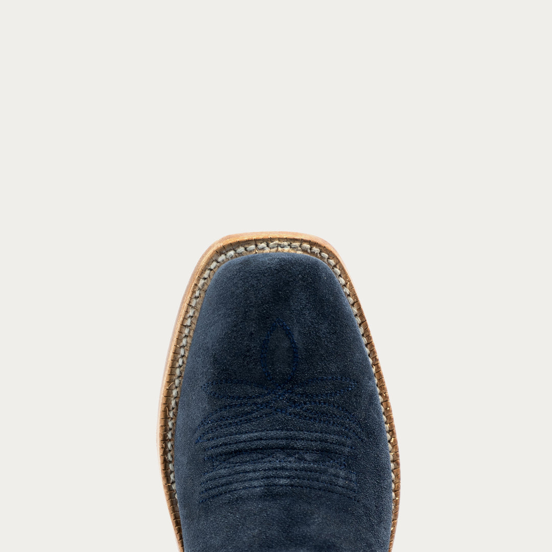 Close-up top view of a navy blue suede boot with a tan leather welt and whipstitching, centered against a light gray background.