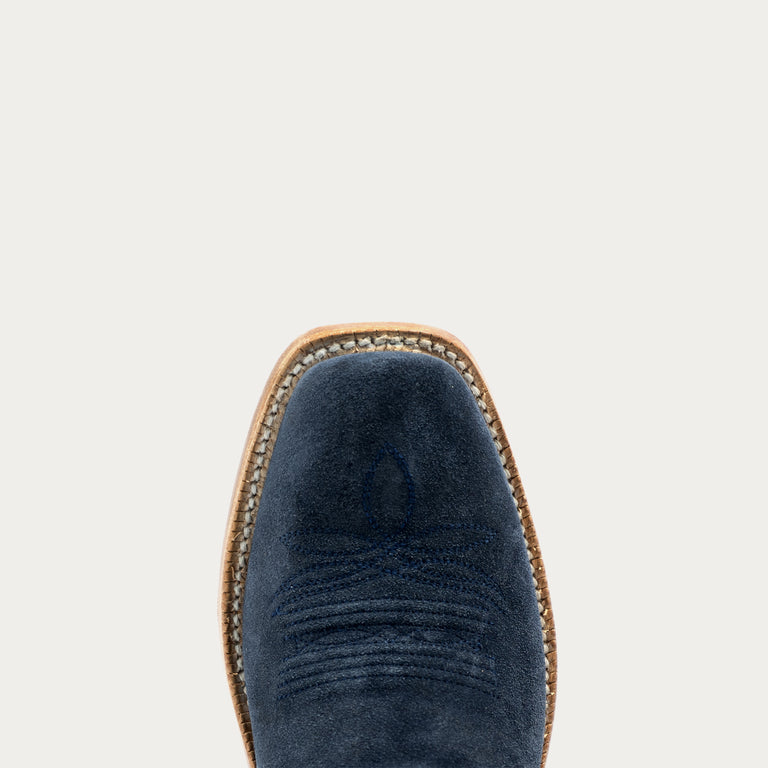 Close-up top view of a navy blue suede boot with a tan leather welt and whipstitching, centered against a light gray background.