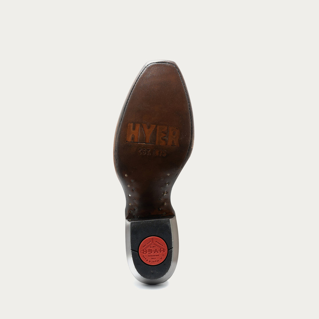 Leather sole of cowboy boot with "HYER" embossed logo on footbed and red heel cap on heel on gray background