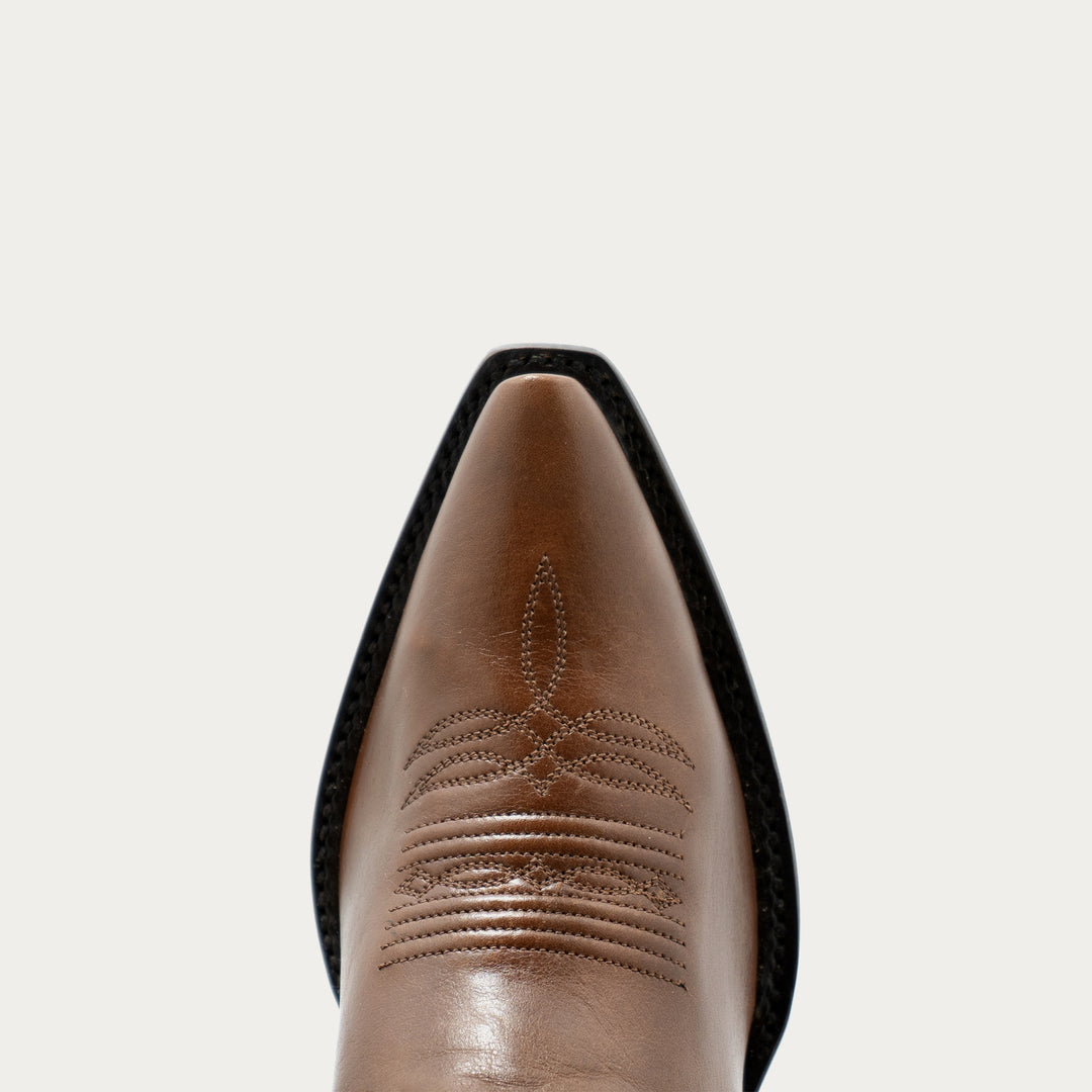 Close-up of a brown leather boot with detailed stitching on a light gray background