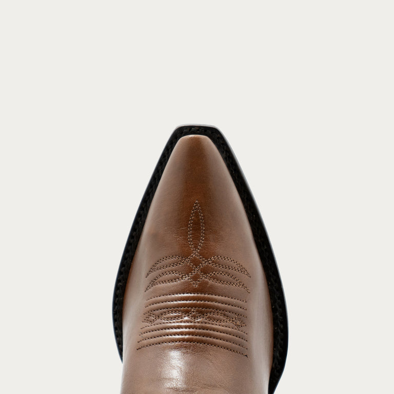 Close-up of a brown leather boot with detailed stitching on a light gray background