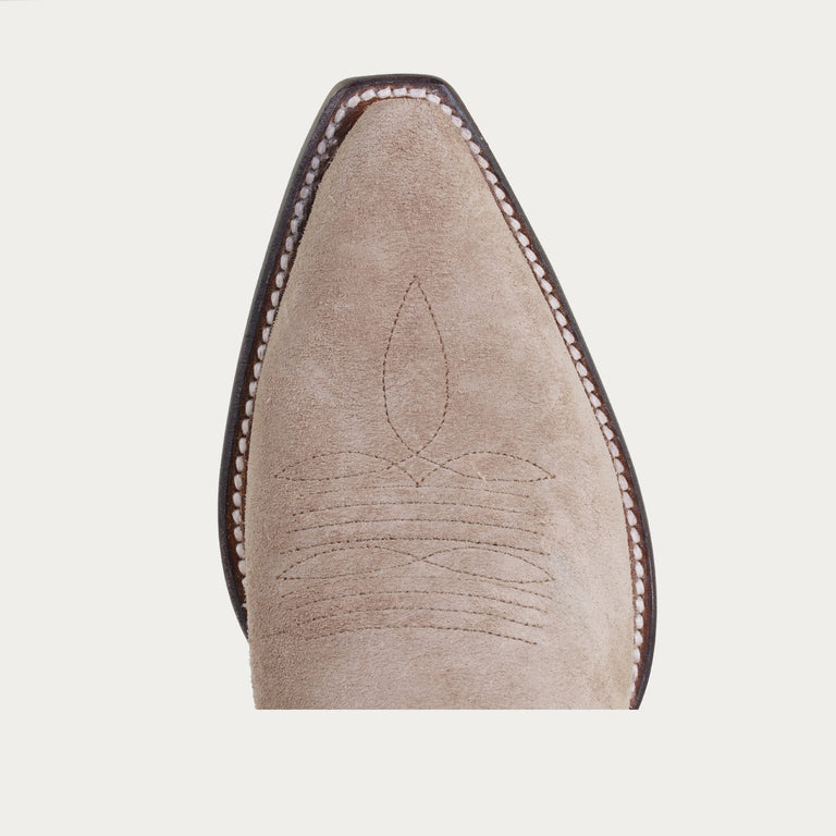 Close-up of a beige suede shoe with brown stitching on a light gray background