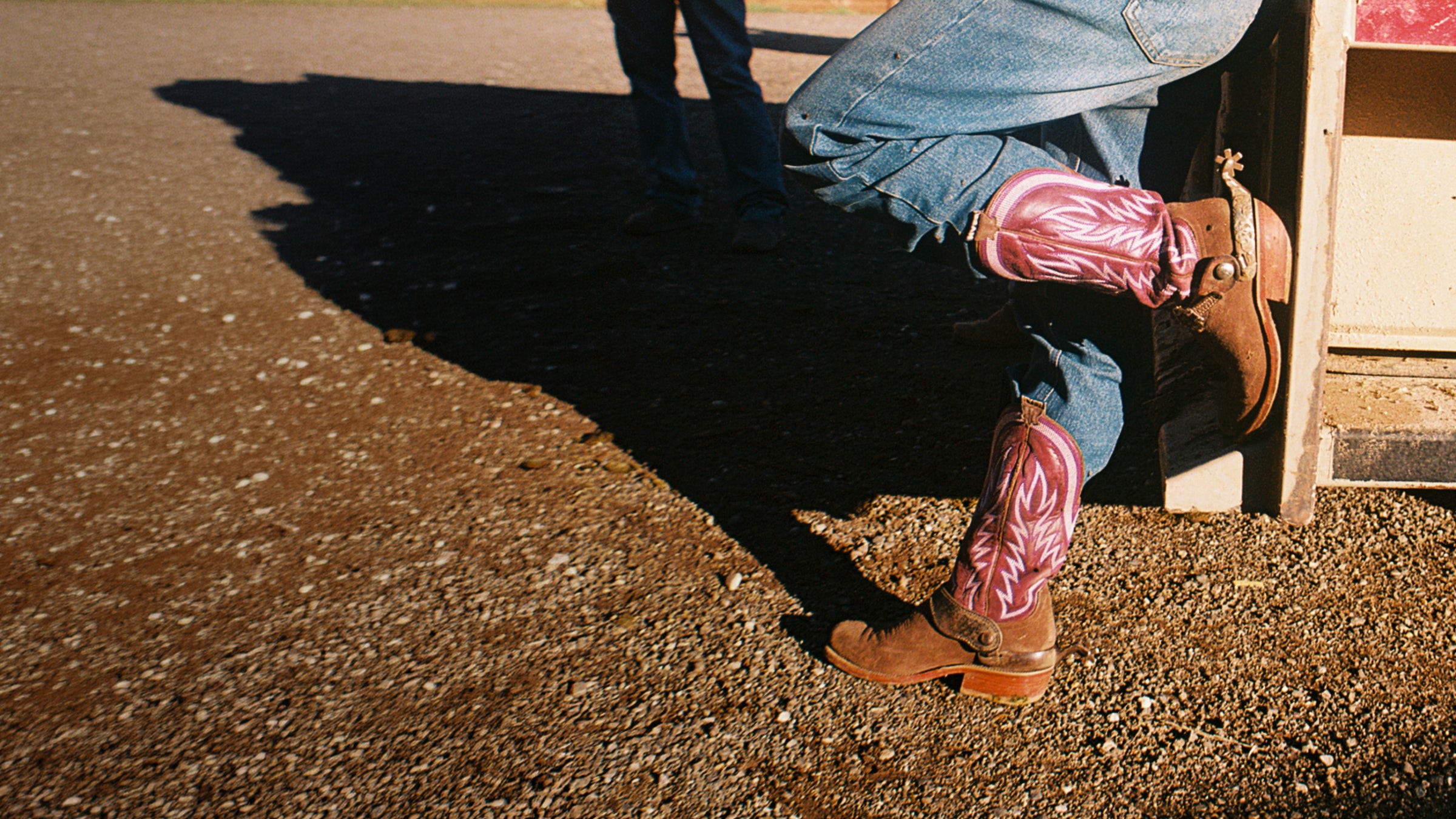 Person wearing cowboy boots stepping onto a wooden platform with a shadow on the ground.