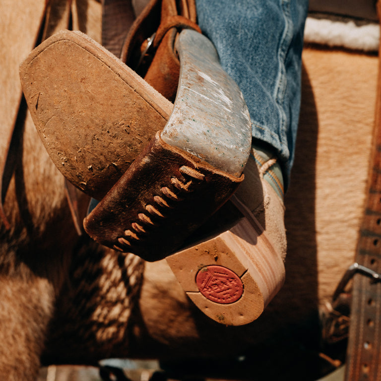 Close-up of brown leather boots with a visible brand logo on a horseback riding saddle.