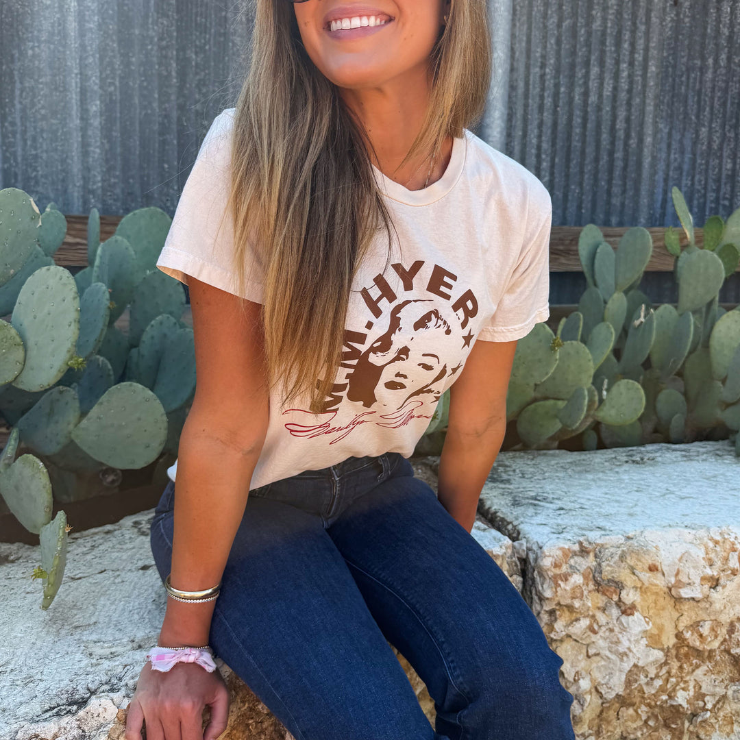Woman wearing a t-shirt with text and graphics, sitting outdoors with cacti in the background