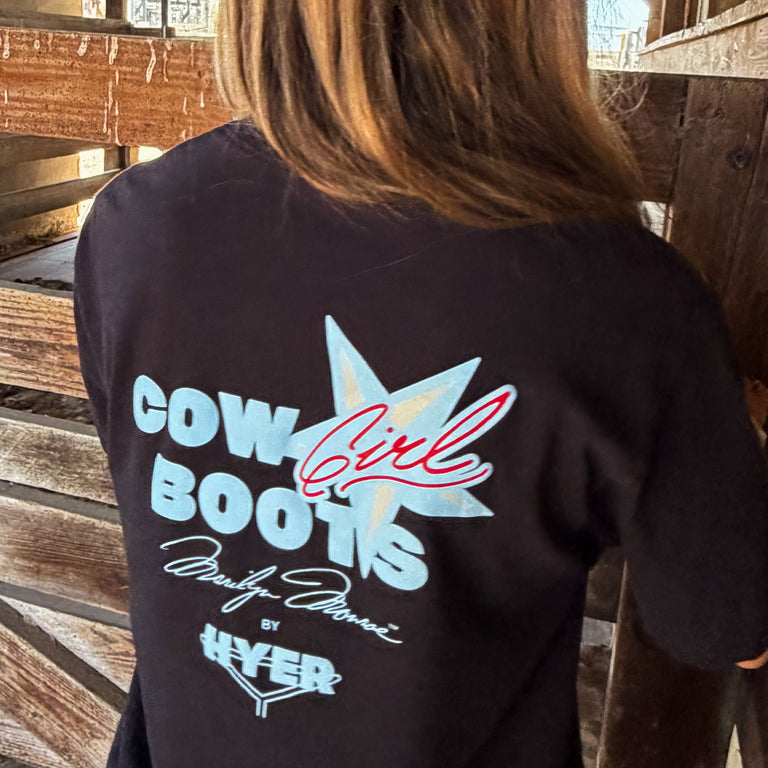 Black t-shirt with 'Cow Girl Boots' design on the back, worn by a person in a wooden setting.