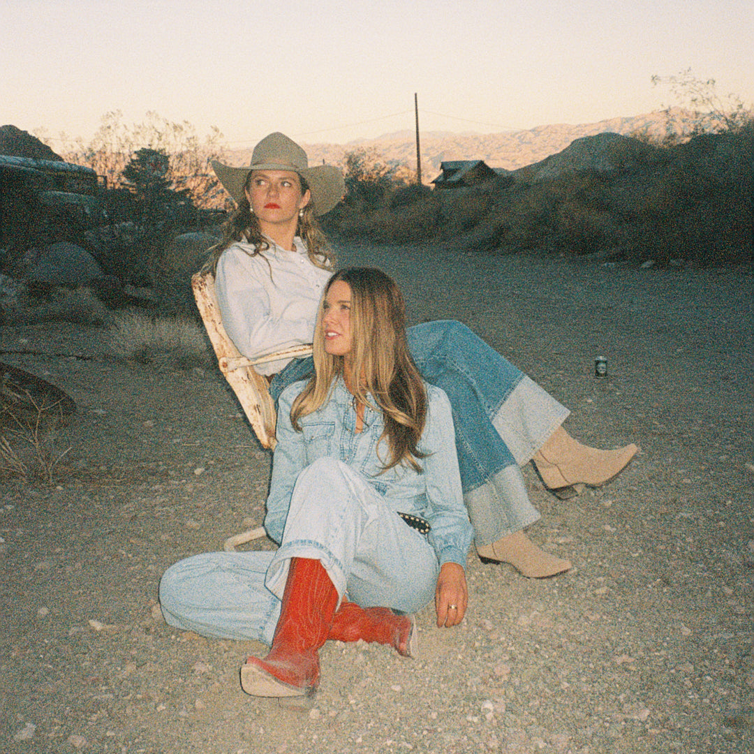 Two women sitting on a dirt road with a scenic background