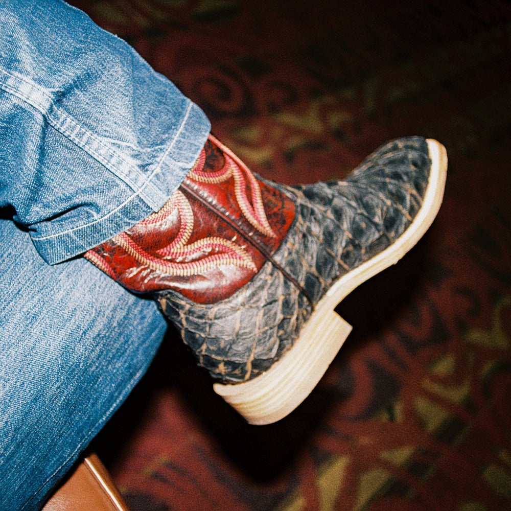 Picture of cowboy boot with dark red shaft and big bass scale vamp with a person wearing blue jeans