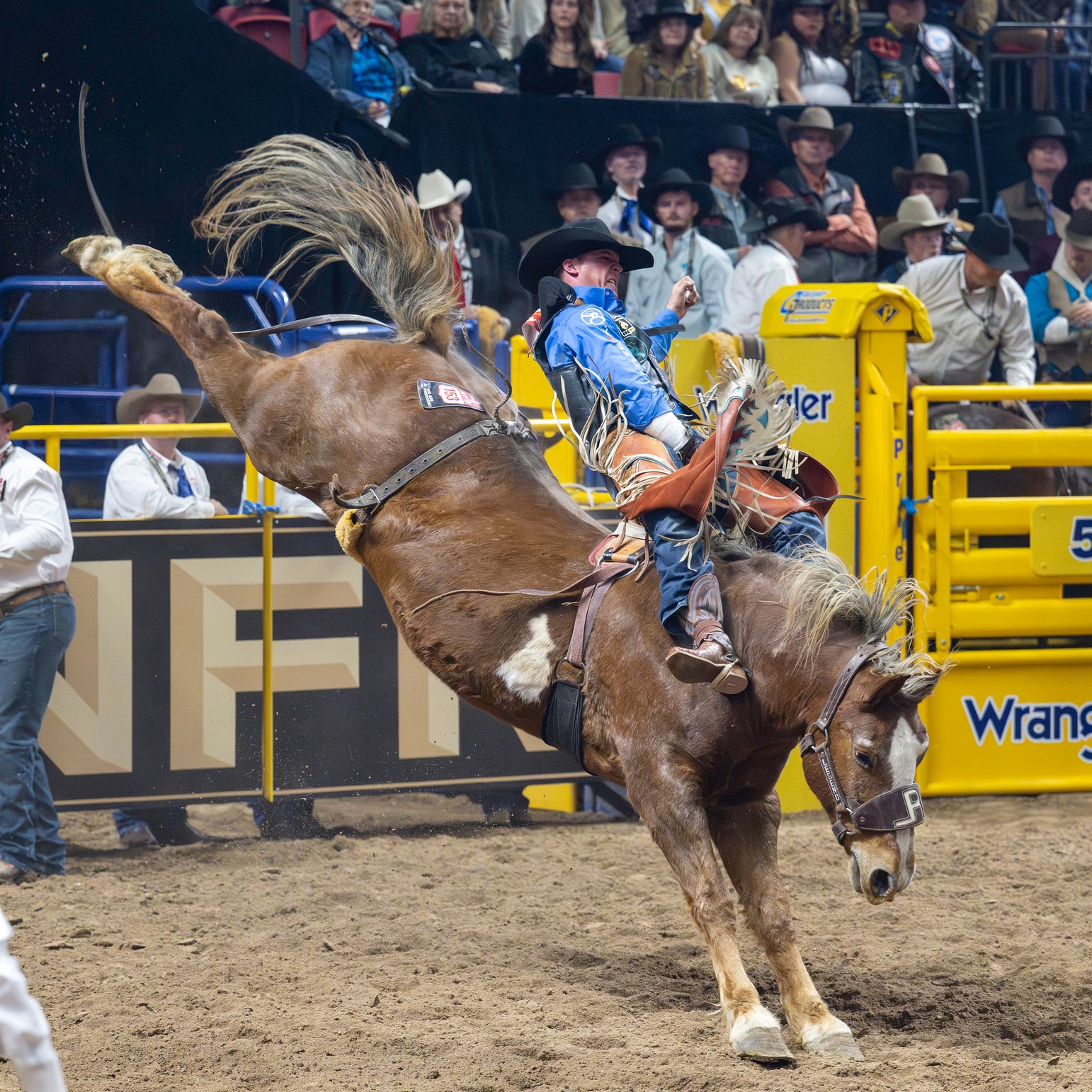 Man competitively riding a horse at a rodeo with spectators in cowboy hats watching in the stands