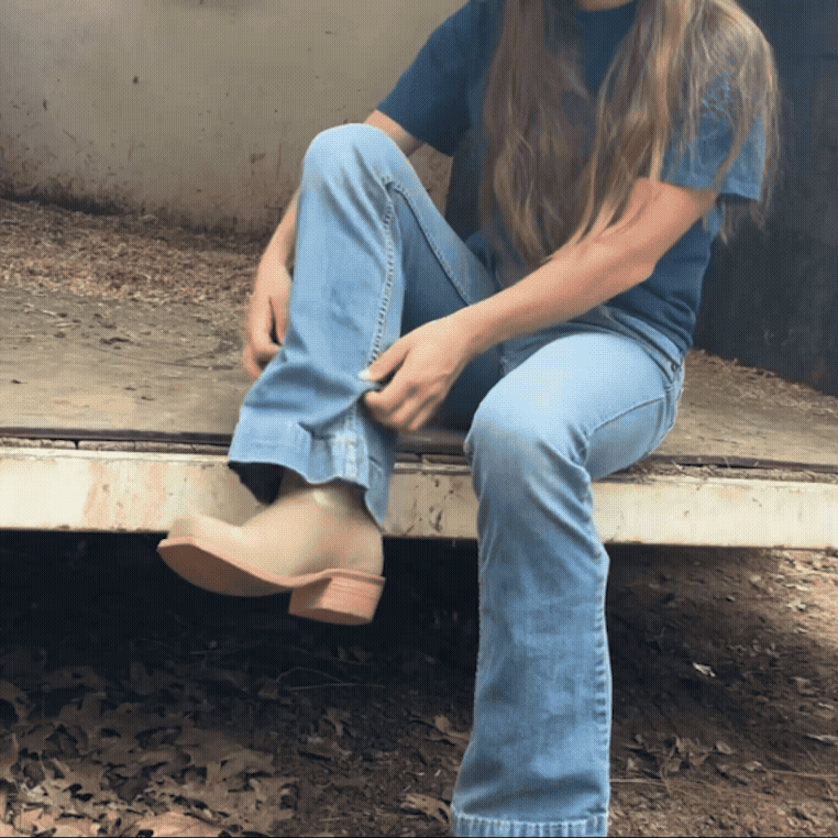 Gif of woman sitting on a trailer bed pulling up jean leg to show mint green and tan cowboy boot